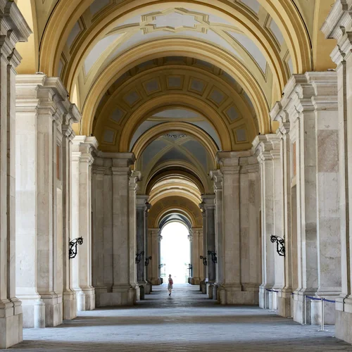 Hotel vicino alla Reggia di Caserta · Regina 4★ Galleria con archi e colonne in marmo con soffitto decorato e persona sullo sfondo