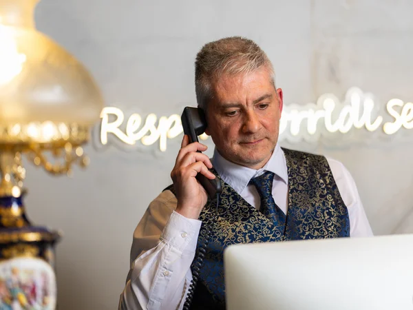 Hotel vicino alla Reggia di Caserta · Regina 4★ Receptionist in gilet elegante risponde al telefono davanti al computer