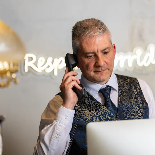 Hotel vicino alla Reggia di Caserta · Regina 4★ Receptionist in gilet elegante risponde al telefono davanti al computer