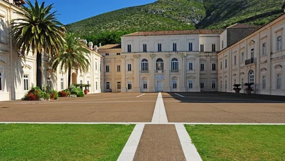 Hotel Regina Caserta · 4 stelle · A due passi dalla Reggia Cortile con edificio storico bianco e palme davanti a una montagna verde