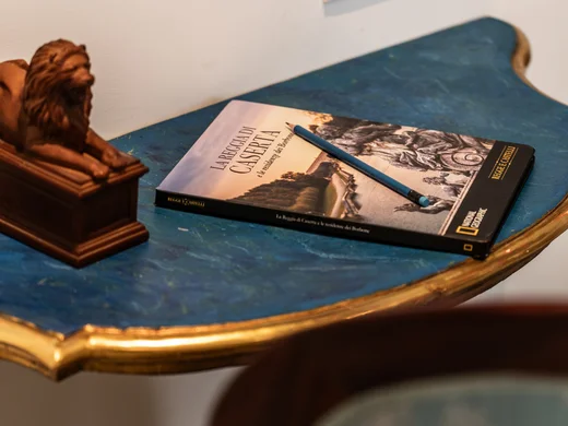 Hotel vicino alla Reggia di Caserta · Regina 4★ Tavolino blu con libro, matita e statuetta di leone, sedia azzurra decorata