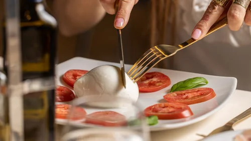 Hotel vicino alla Reggia di Caserta · Regina 4★ Persona che taglia mozzarella circondata da fette di pomodoro e basilico su piatto bianco