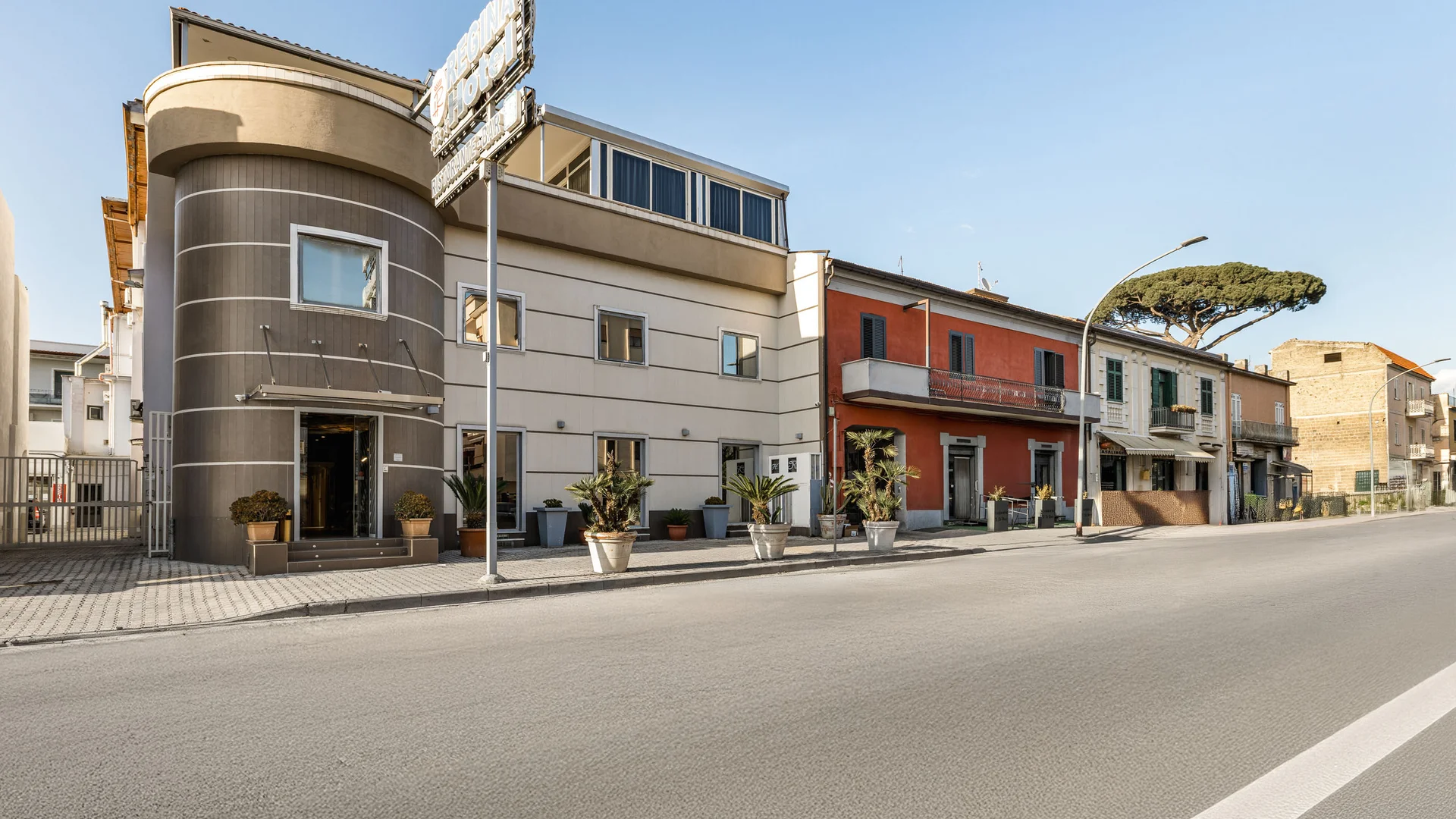 Hotel Regina Caserta · 4 stelle · A due passi dalla Reggia Facciata moderna di un hotel con piante in vaso lungo la strada